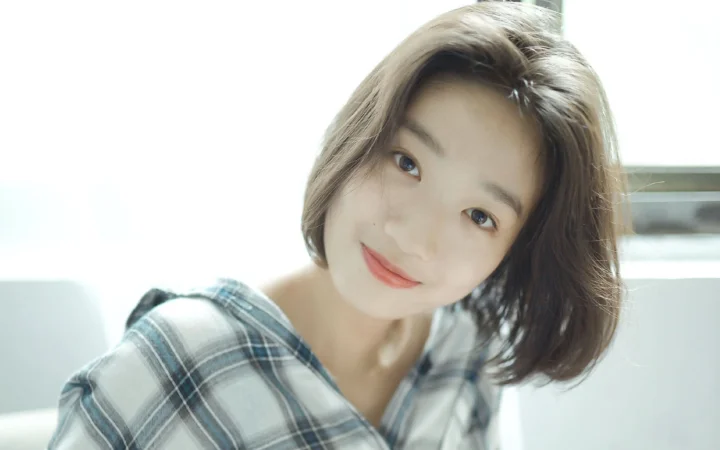 一名成年女性穿着格纹上衣，在明亮的室内靠近镜头微笑。