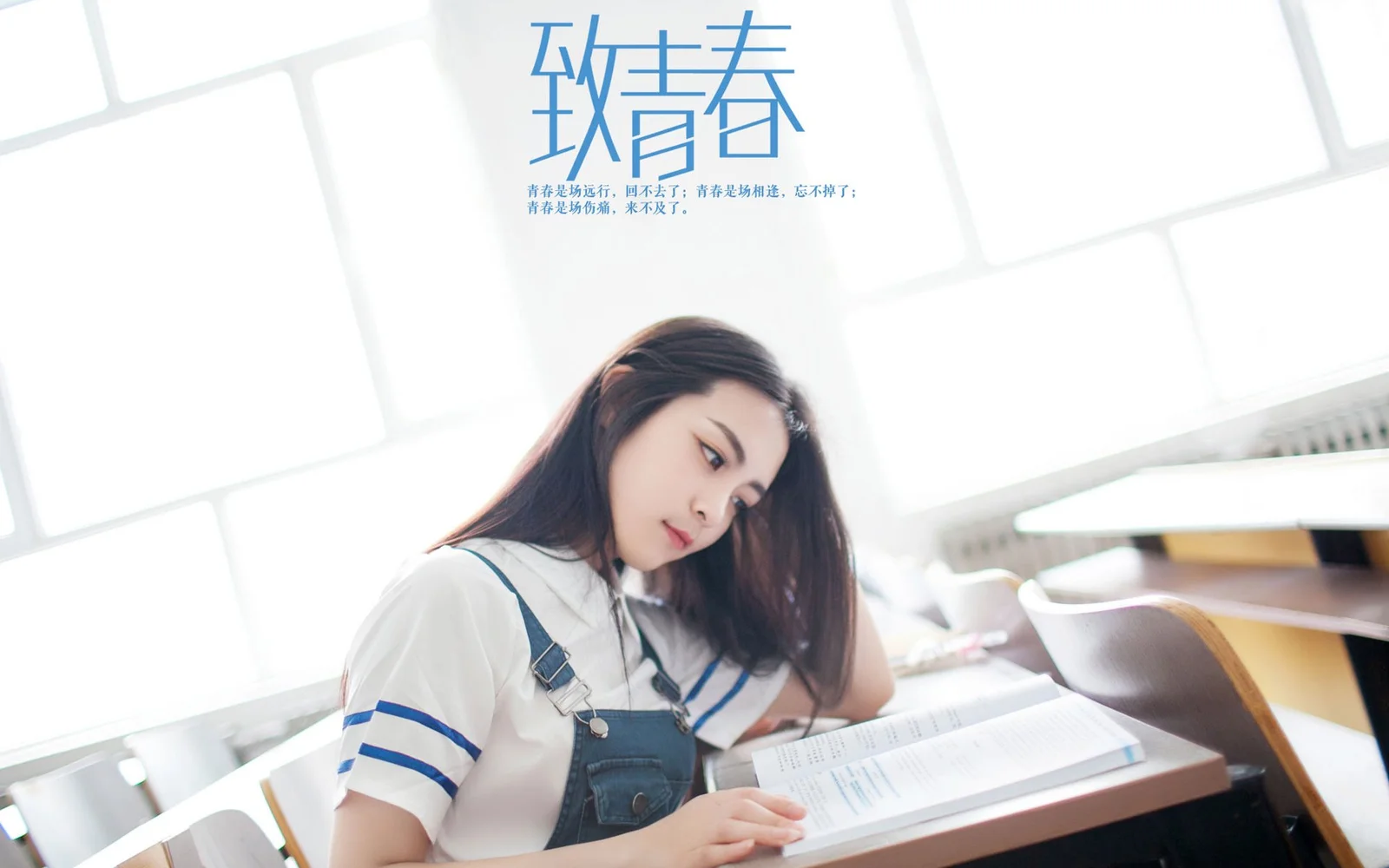 一名年輕女子坐在窗邊的課桌前翻閱書本。