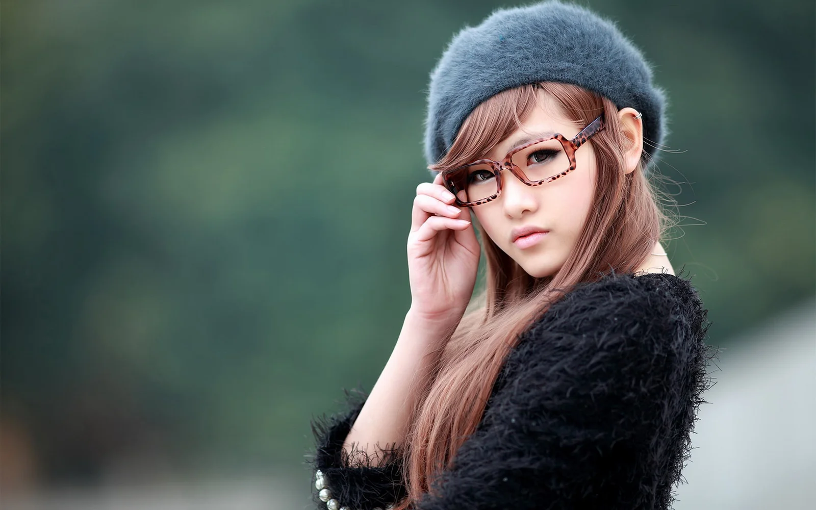 眼鏡とグレーのベレー帽を身につけた女性が、ぼやけた屋外の背景の前に立っています。