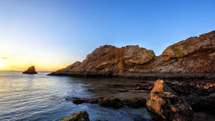 夕阳映照下的岩石海岸与平静海面构成开阔的自然景观。