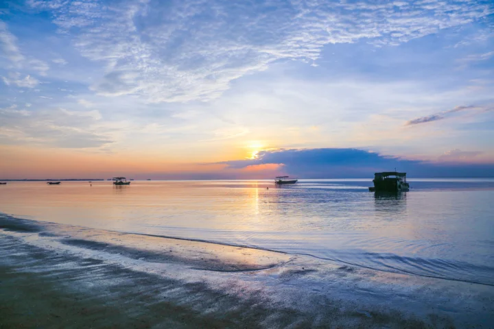 夕阳映照着宁静的海面、沙滩和远处的小船。