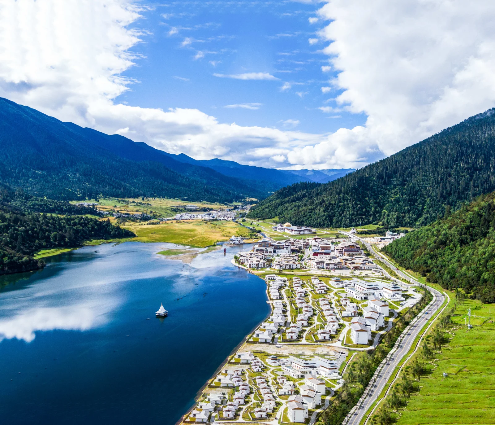 湖泊、森林覆盖的群山、云朵与湖畔小镇构成一幅开阔的山谷风景。