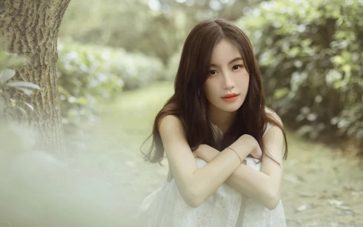 一位长发女子在树木环绕的林间面向镜头，双臂交叠于胸前。