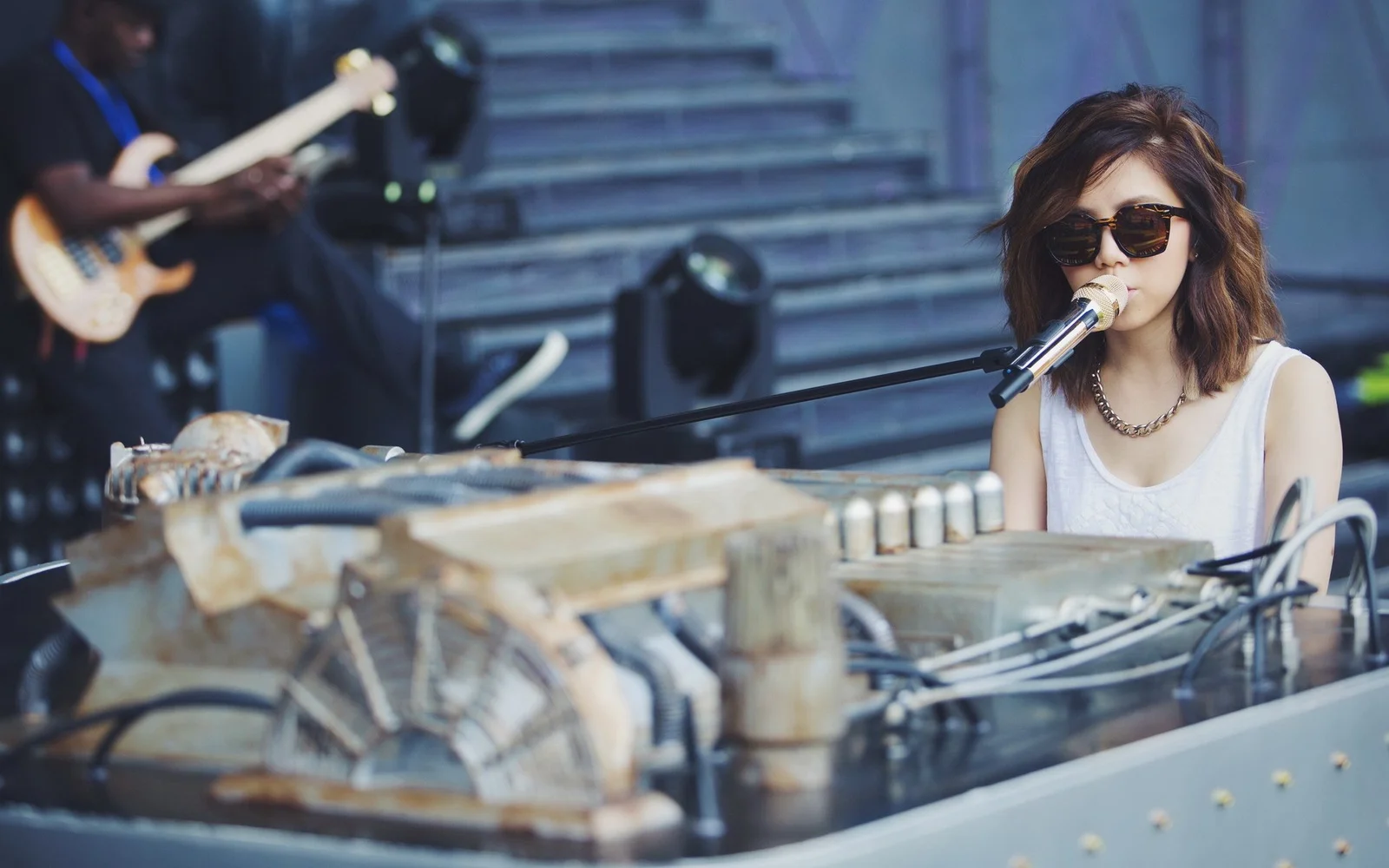 サングラスをかけた成人女性がキーボードの前でマイクに向かって歌っている。