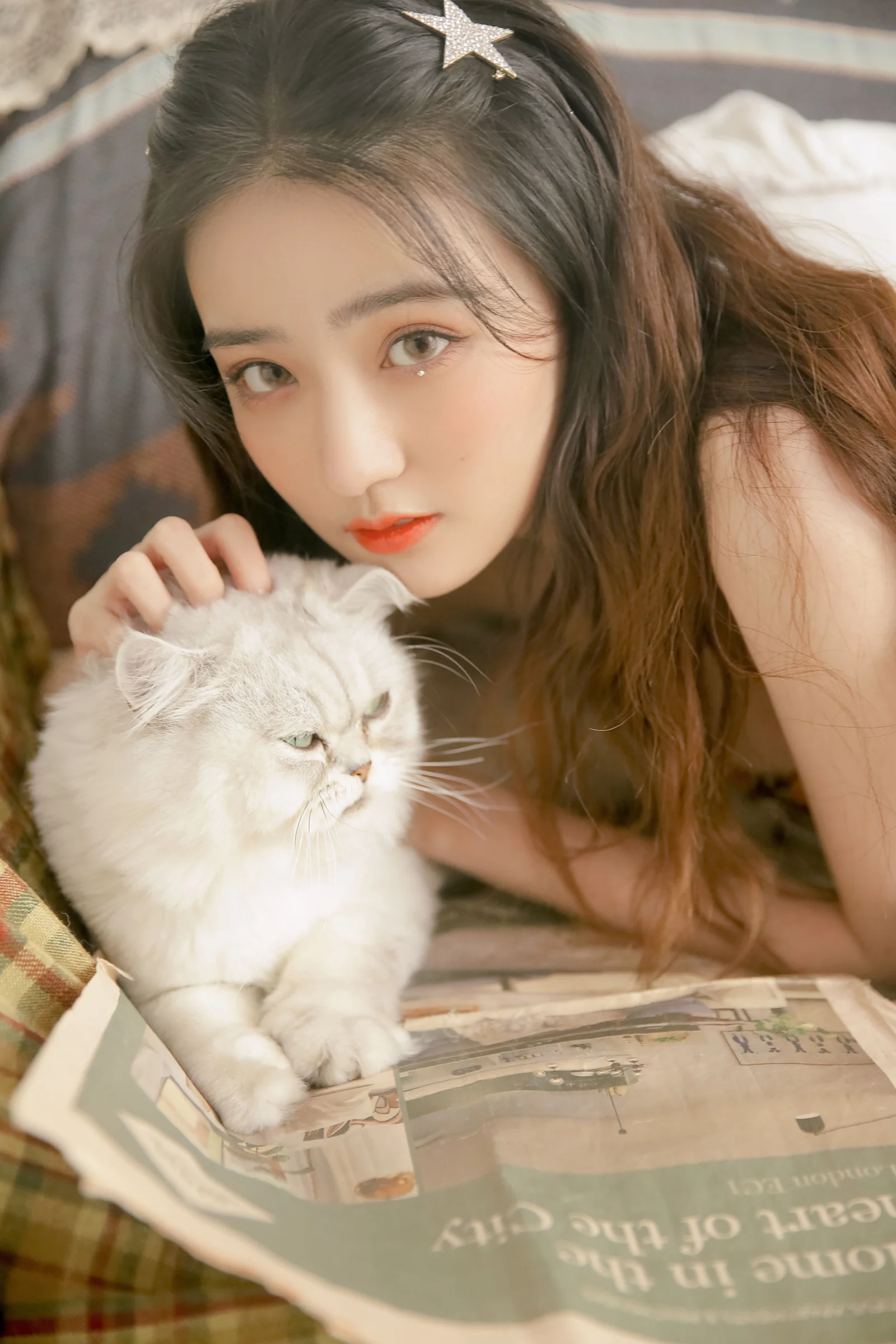 긴 머리의 여성이 글자가 인쇄된 종이 위에서 복슬복슬한 흰 고양이에게 가까이 다가가 있다.