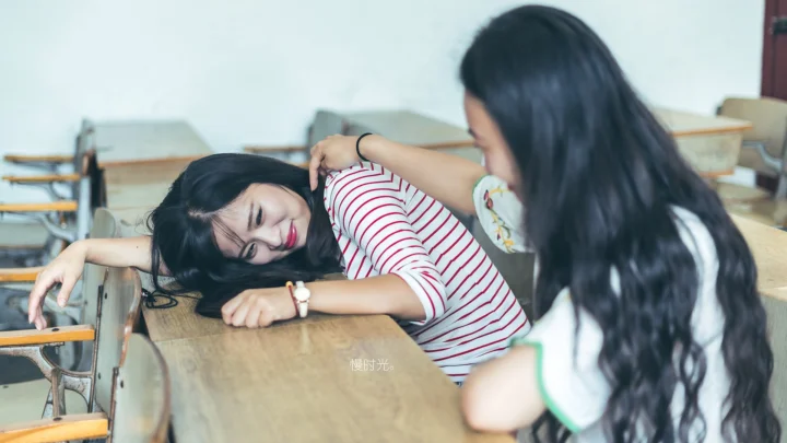 两名女性在教室的课桌旁互动。