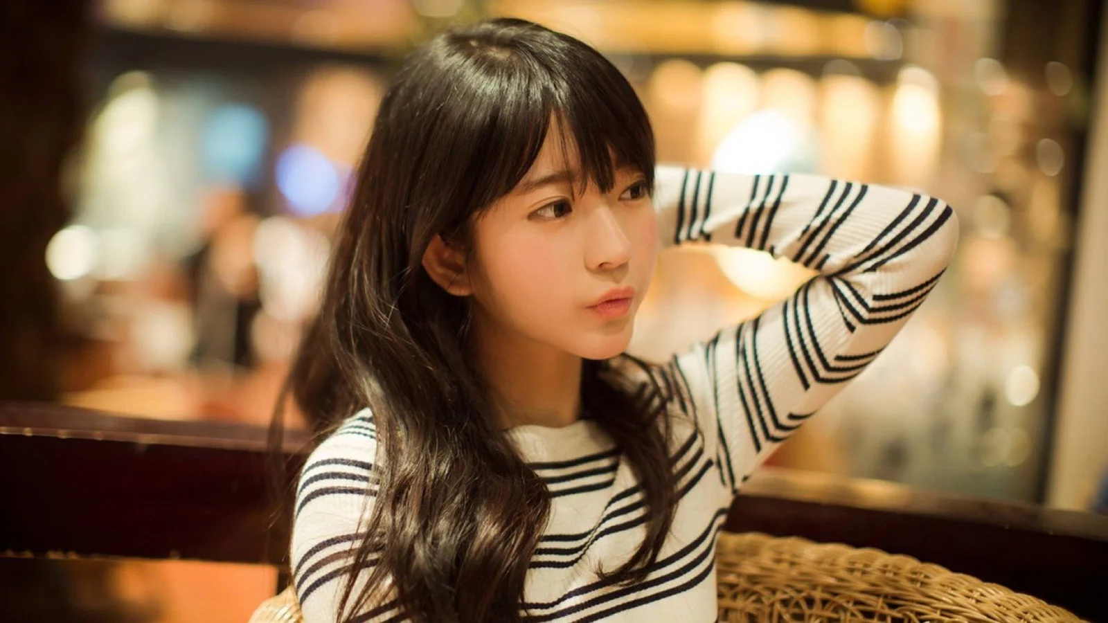 一名长发女性穿着黑白条纹衫坐在温暖灯光的室内环境中。