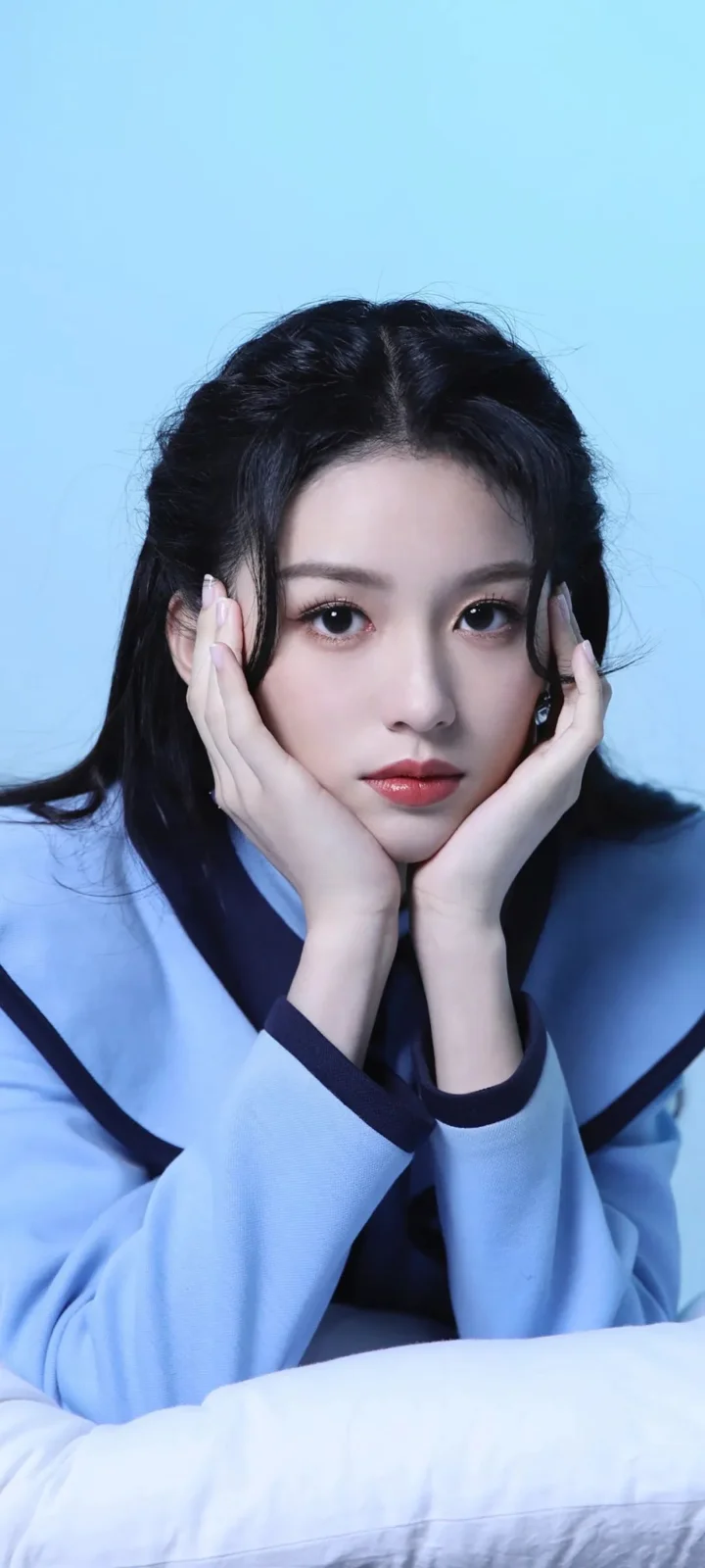 一名成年女性在浅蓝色背景前托腮注视镜头。