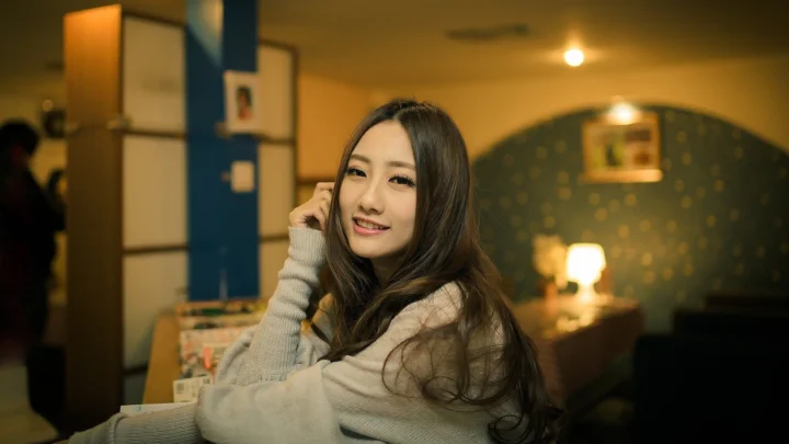 一名成年女性坐在温暖灯光下的室内环境中，面向镜头微笑。