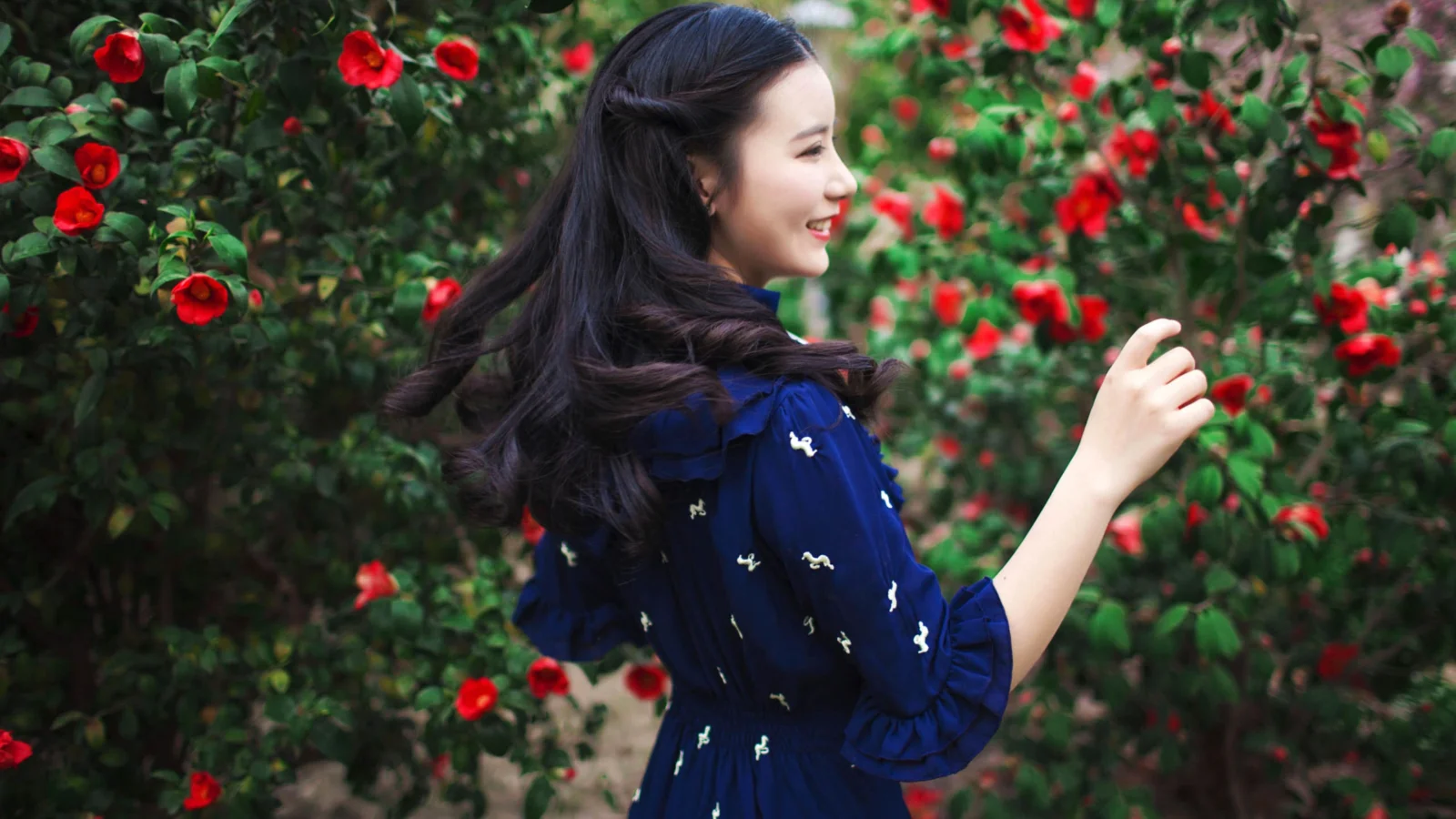 一名女子站在开满红花的花园中。