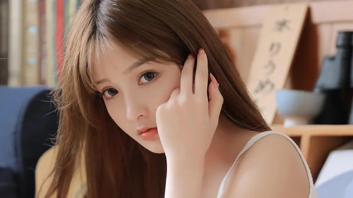 一名长发女性在室内面对镜头并用手触碰侧脸。