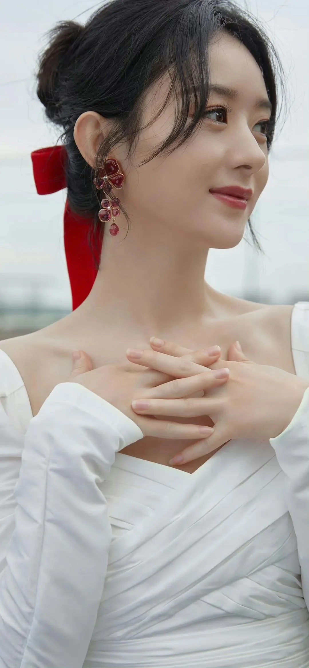 一位身穿白色礼服的女性在户外背景前侧身微笑。