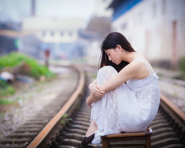一名身穿白色连衣裙的成年女子坐在铁轨上低头休息。