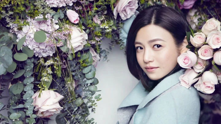 一名成年女性置身于粉白色花朵与绿叶之间。