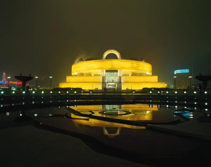 夜晚灯光映照下的城市建筑倒映在广场水面上。