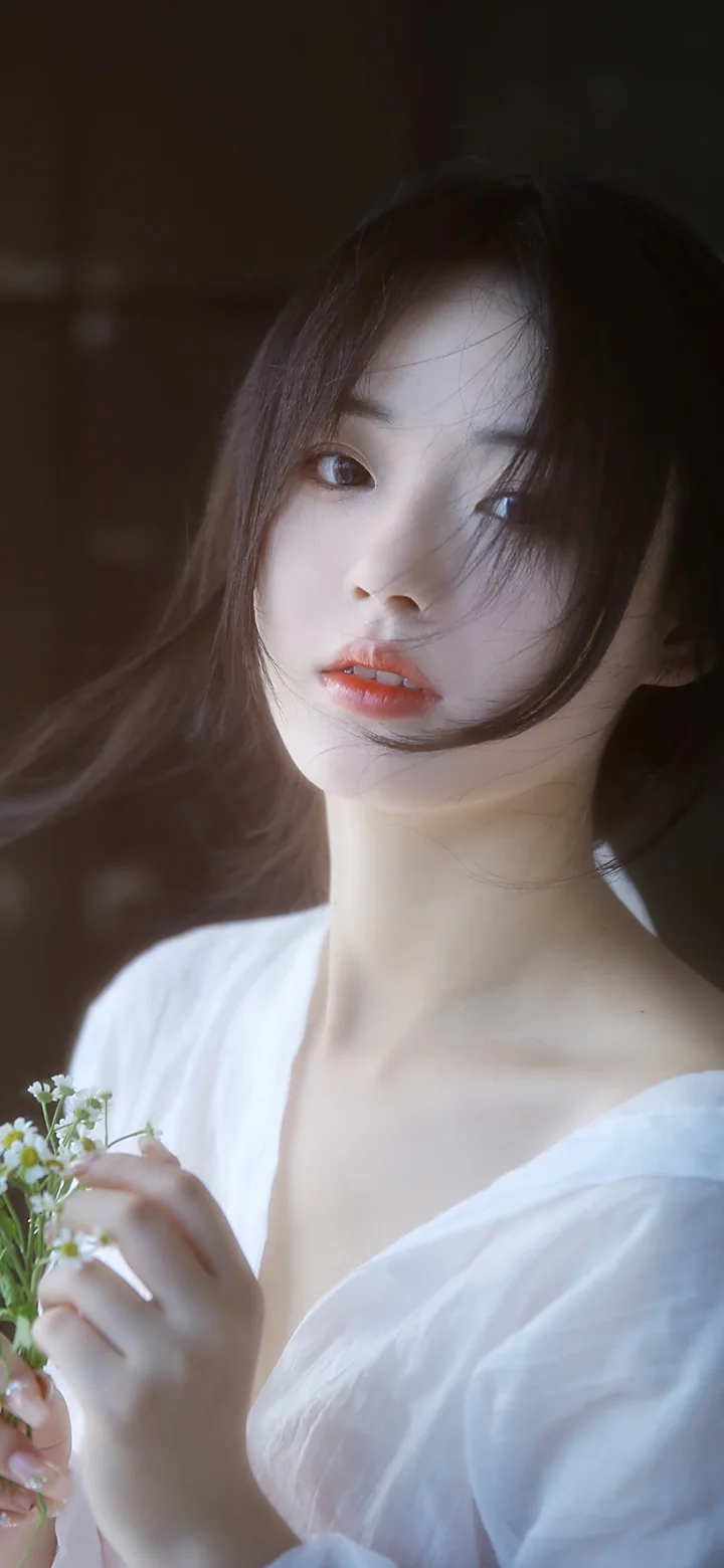 一名长发女子穿着白色上衣，手持小花进行近距离肖像拍摄。