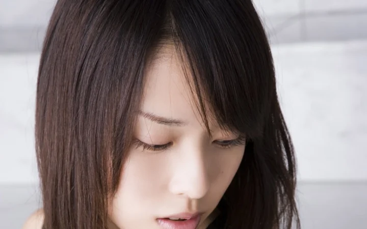 一名深色長髮女性低頭閉眼的近距離人像，背景為淺色調。