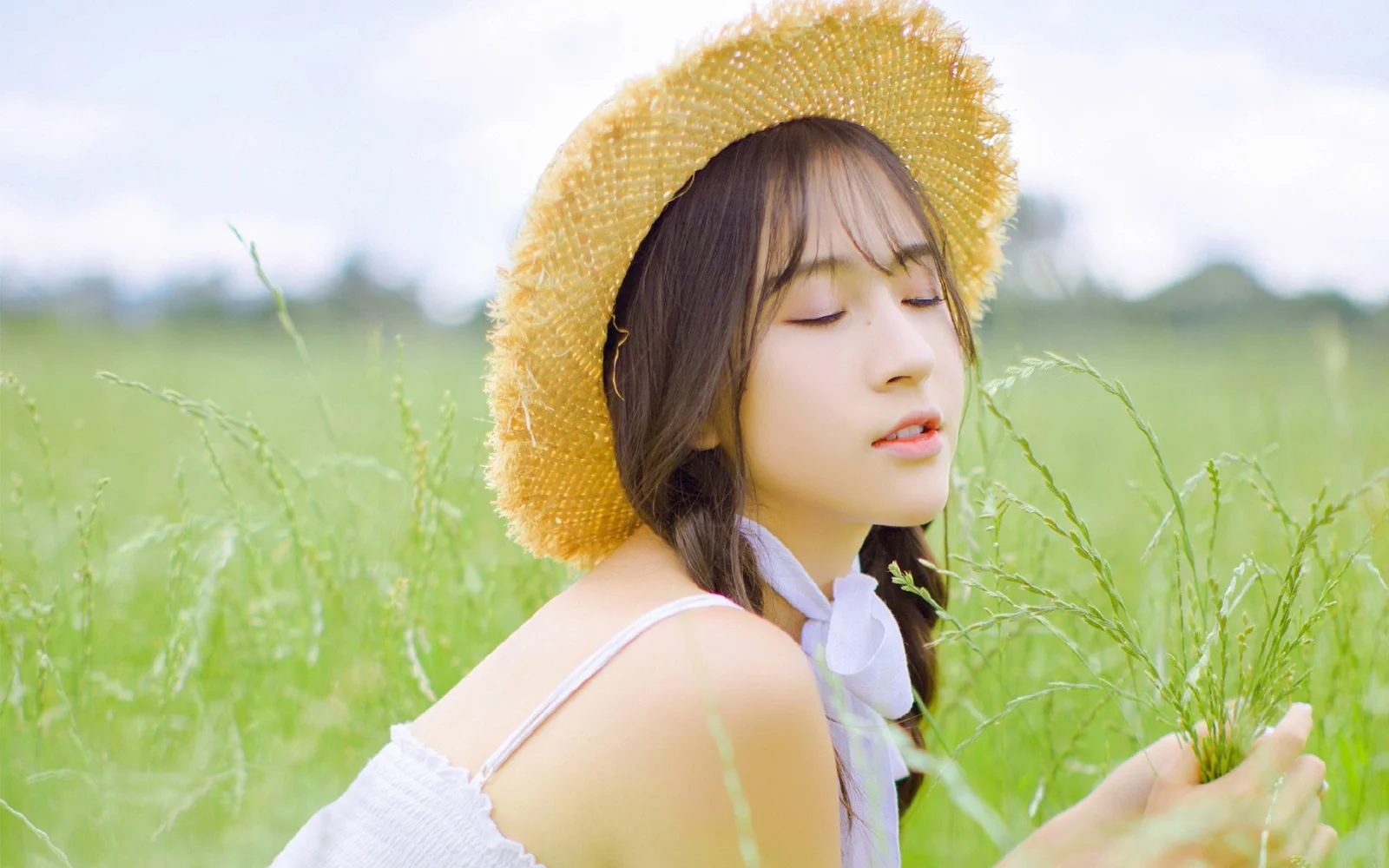 一名戴草帽的女子閉眼站在綠意盎然的草地中。