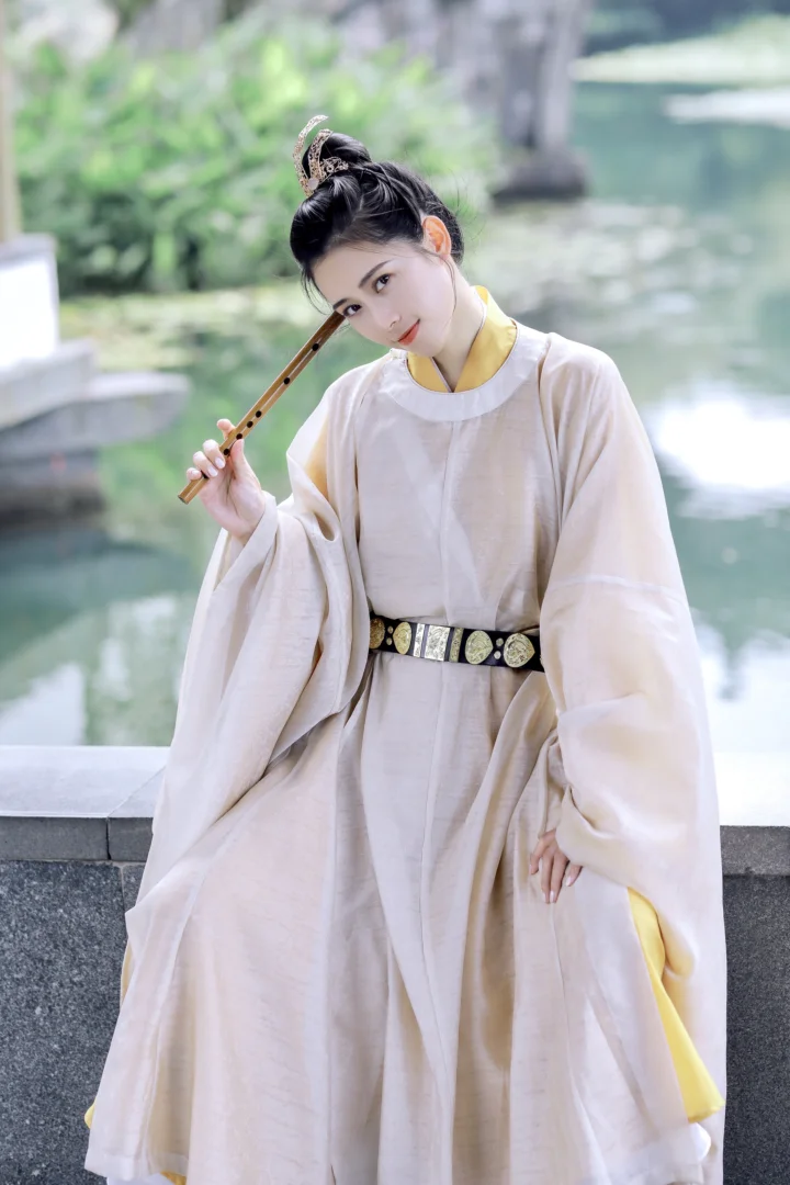 一名身穿浅色汉服的女子站在池塘边，手持竹笛。
