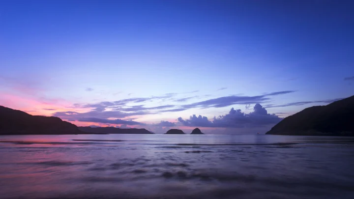 暮色中的海湾映照着粉紫色天空，远处群山与小岛勾勒出宁静的海岸线。