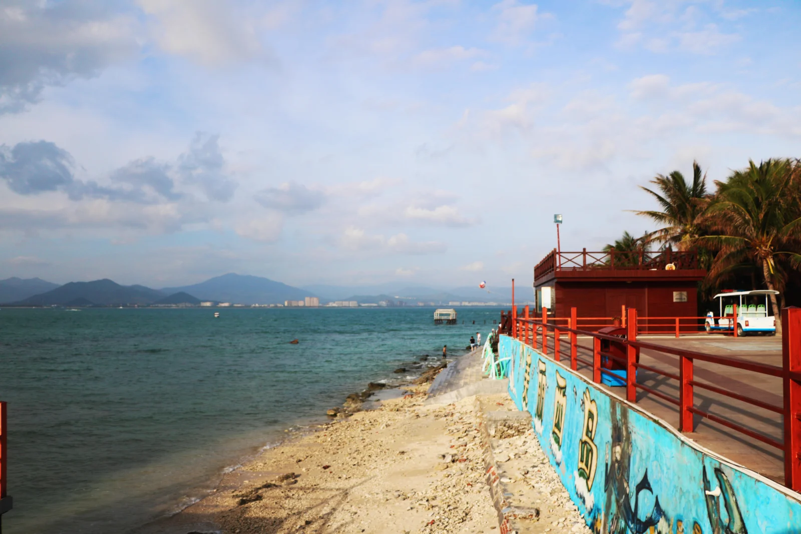 海湾海滩、远山、棕榈树和临海红色平台构成明亮的海岸风景。