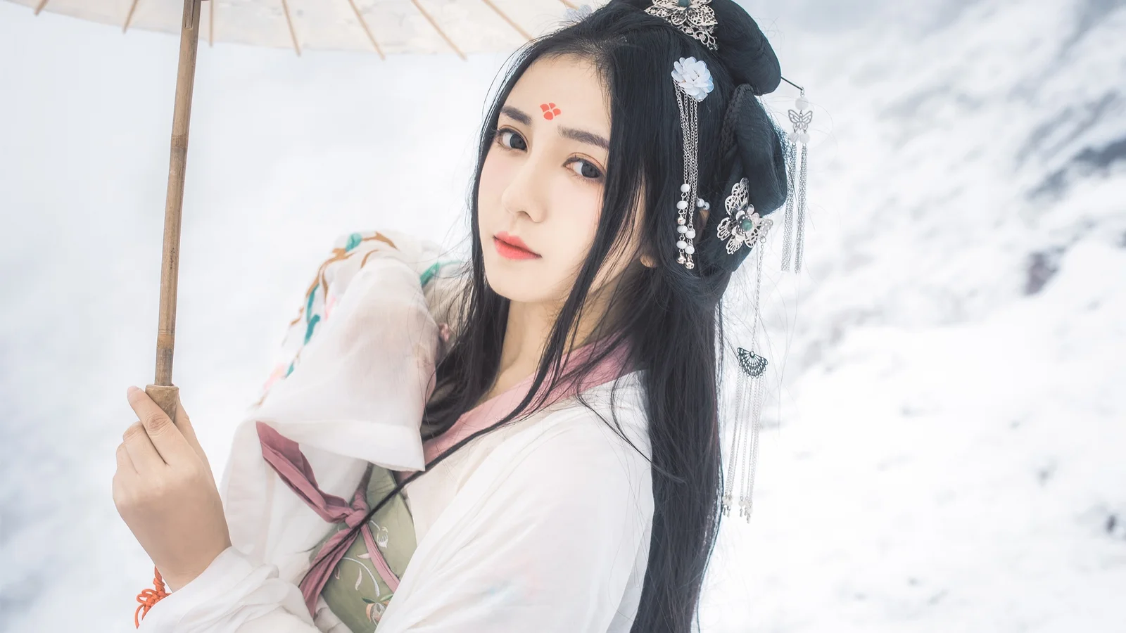 전통 의상을 입은 여성이 눈 덮인 배경 앞에서 우산을 들고 서 있습니다.