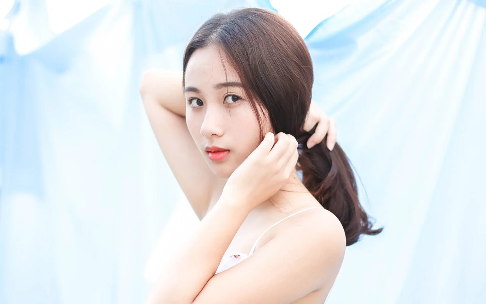 一名成年女性在淺藍色背景前整理頭髮並看向鏡頭。