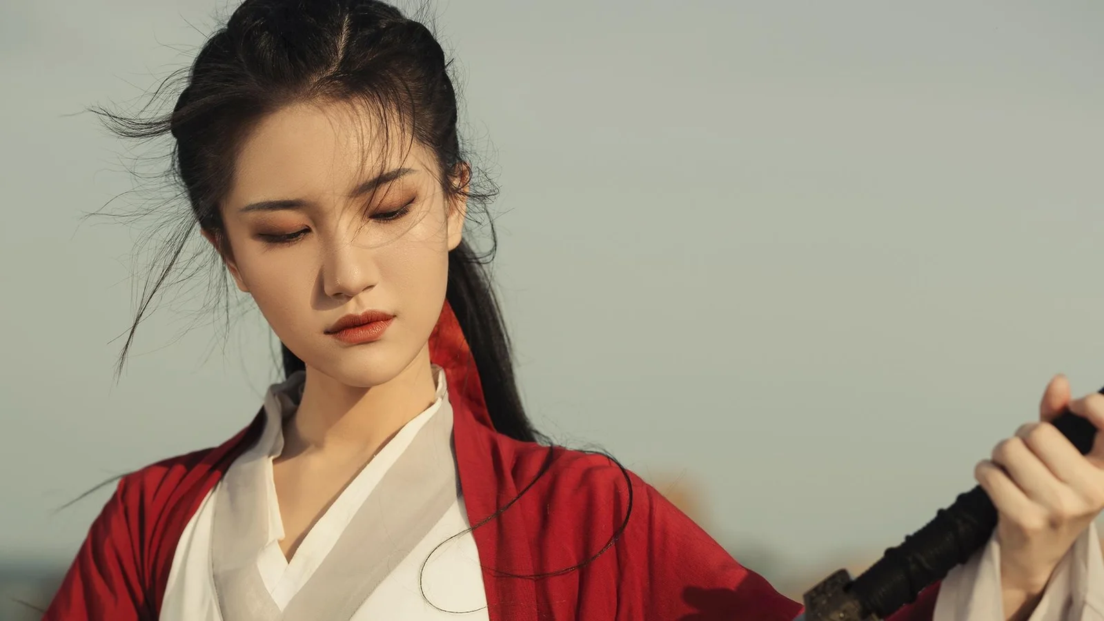一名身穿红色传统风格服装的女子手持剑柄，面向画面站立。