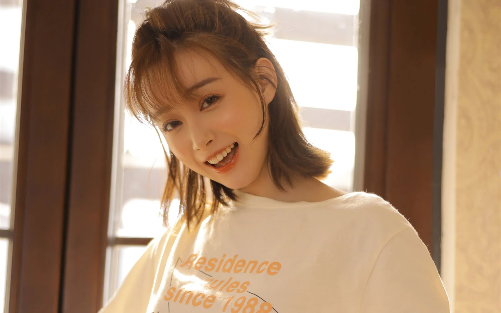 따뜻한 창가의 빛 속에서 성인 여성이 미소 짓고 있는 실내 인물 사진입니다.