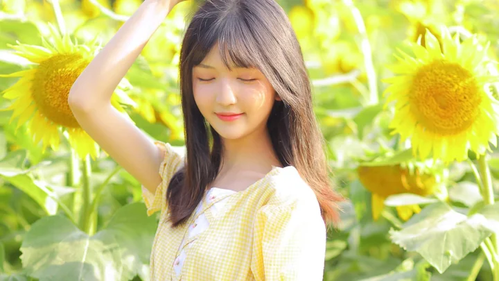 一名身穿黄色格纹上衣的女性站在明亮的向日葵花田中。