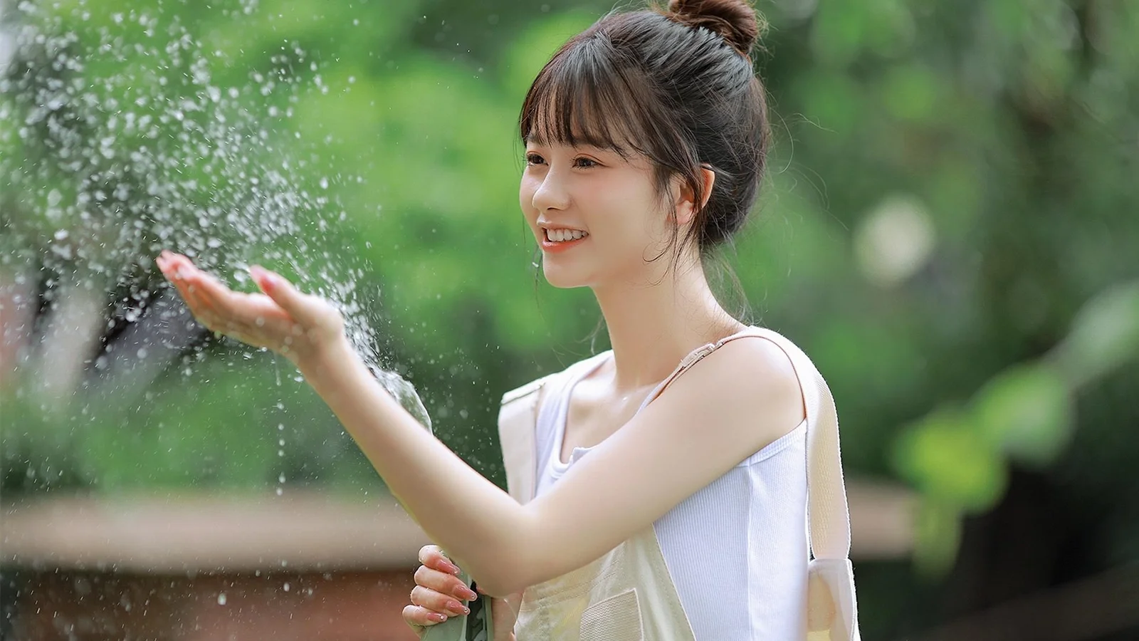 一名成年女性站在绿意盎然的户外环境中，微笑着伸手接住飞溅的水花。