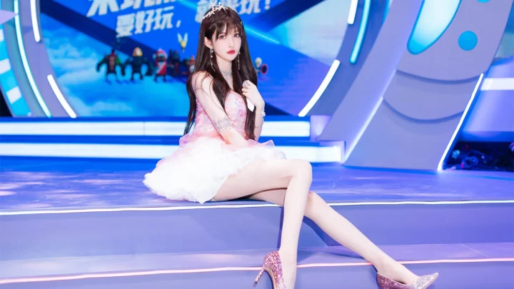 一名穿着粉色连衣裙和高跟鞋的女子坐在明亮的蓝色舞台上。
