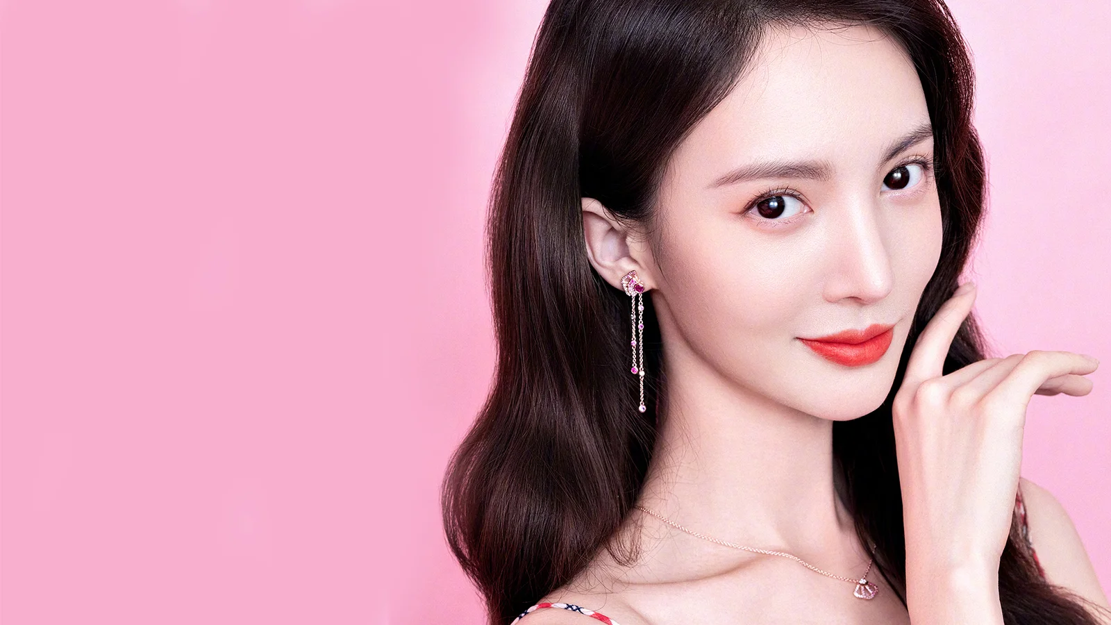 분홍색 배경 앞에서 긴 머리와 정돈된 메이크업을 한 성인 여성이 포즈를 취하고 있습니다.