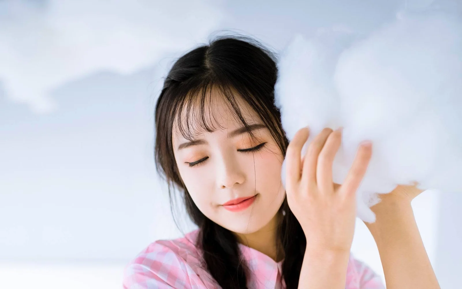 明るく柔らかな背景の前で、成人女性が目を閉じて白い羽根を顔の近くに持っています。