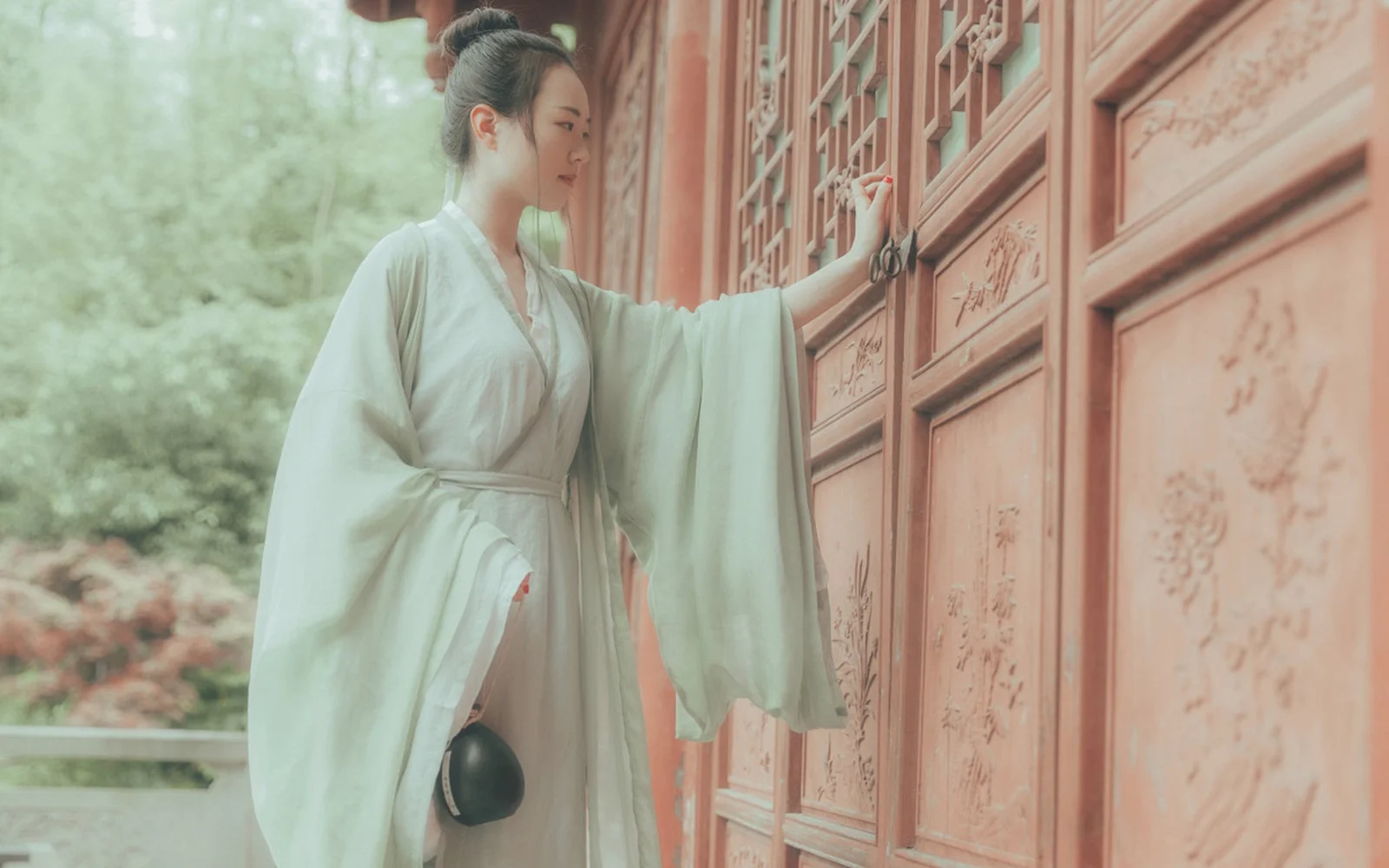 一名身穿浅色传统服饰的女子站在雕花红门前。