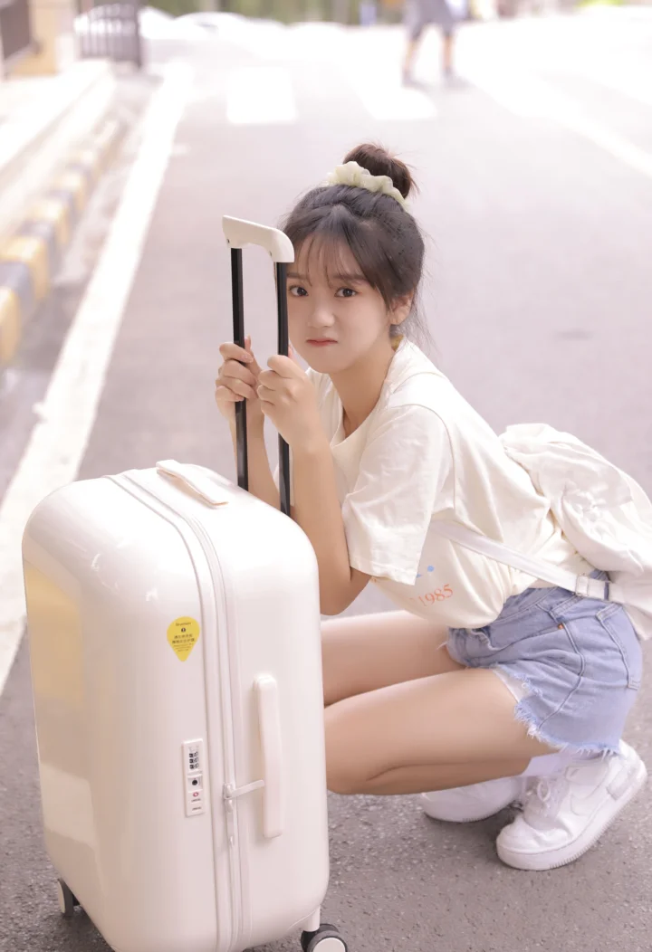 一名年轻女子蹲在街边，手扶着白色行李箱。