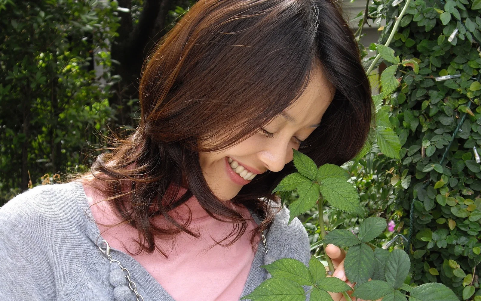 女性が緑の植物のそばでうつむいて微笑み、葉にそっと触れている。