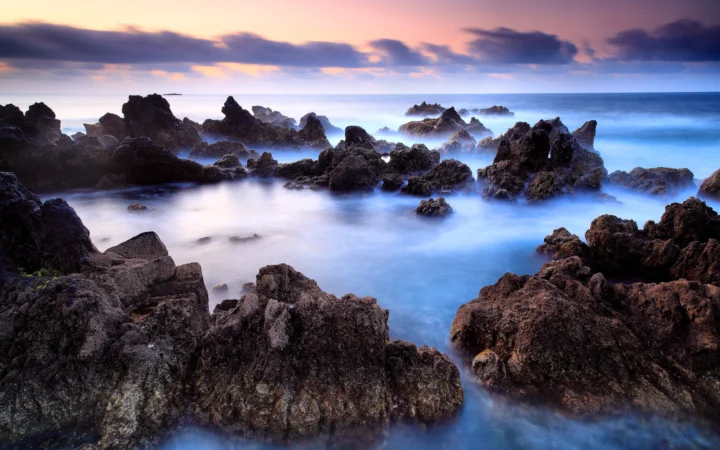 夕阳映照下，海水环绕着崎岖的黑色礁石海岸。