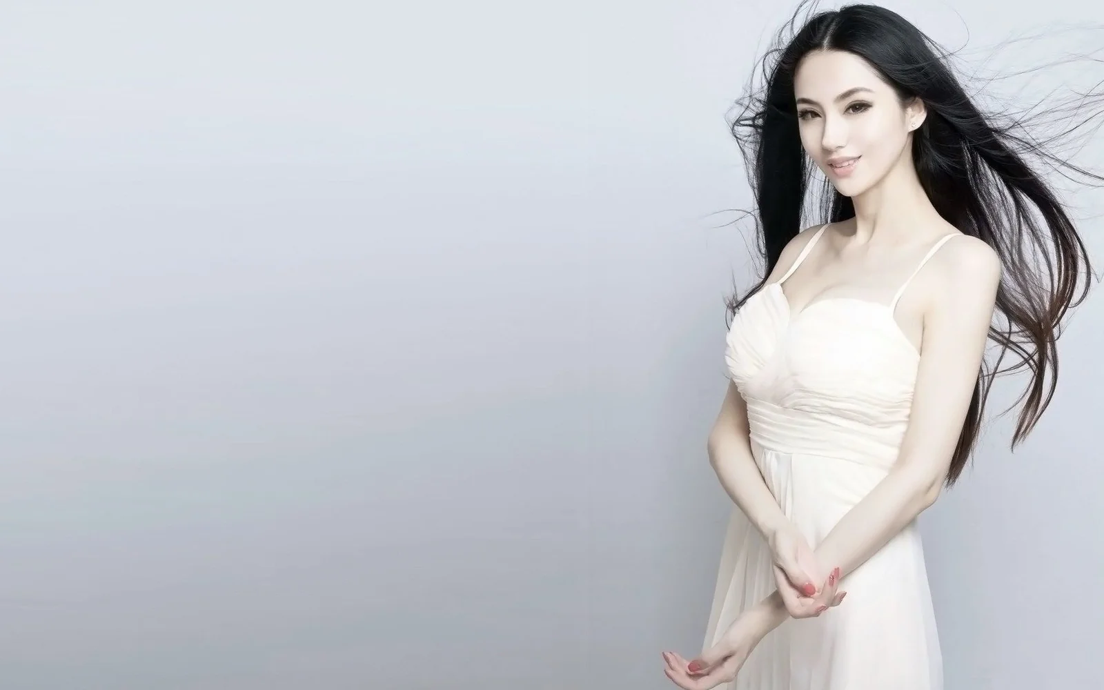 一名身穿白色连衣裙的女性站在浅灰色背景前。