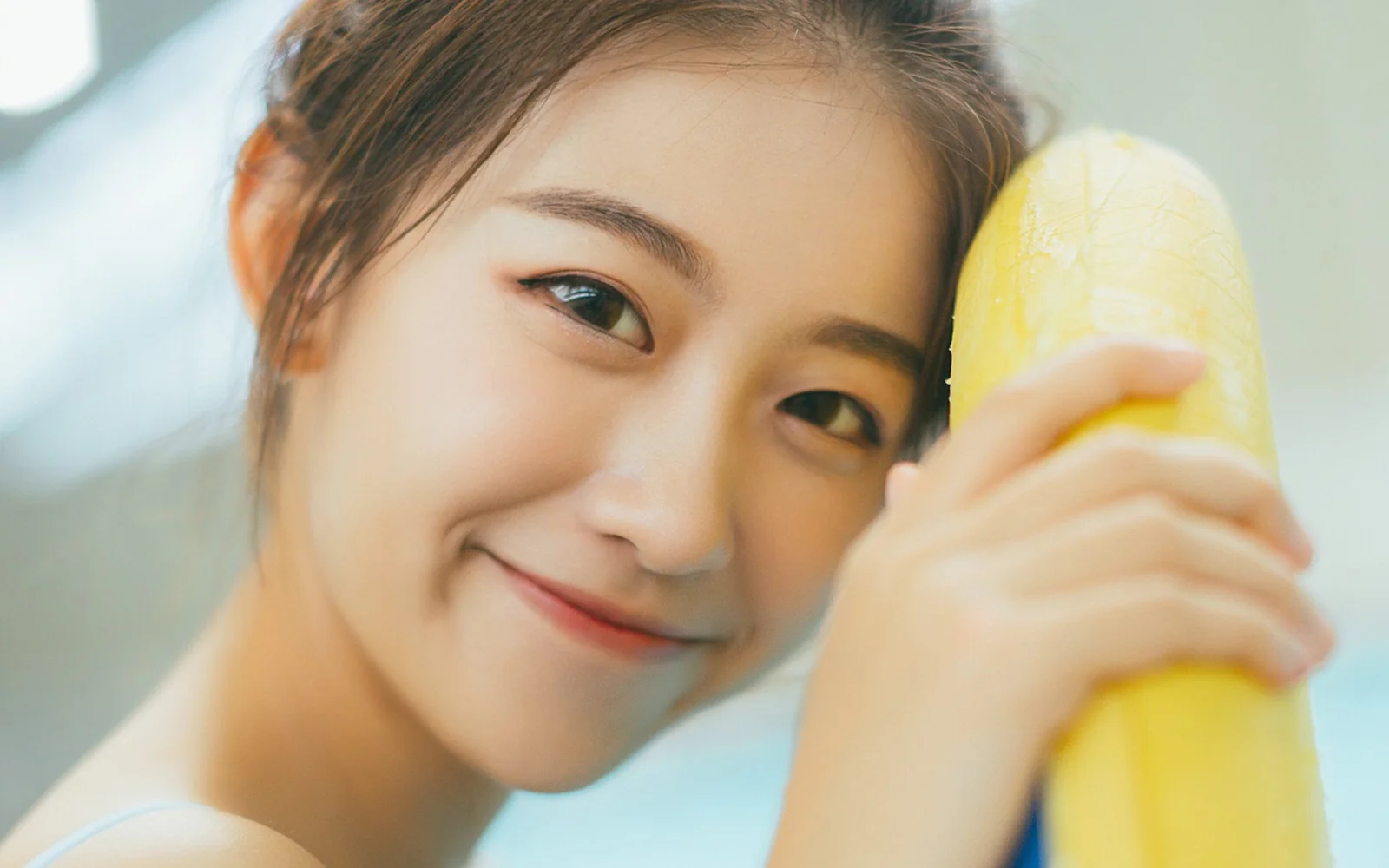 미소 짓는 성인 여성이 노란색 물체를 손에 들고 가까이에서 카메라를 바라보고 있다.