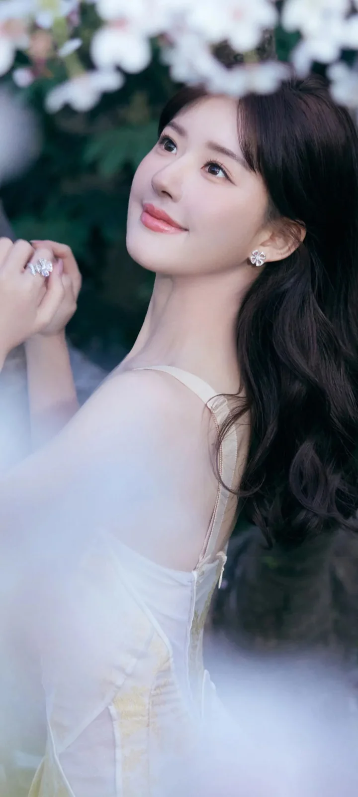 一位长发女性身穿白色礼服，在朦胧花影与雾气中回眸微笑。