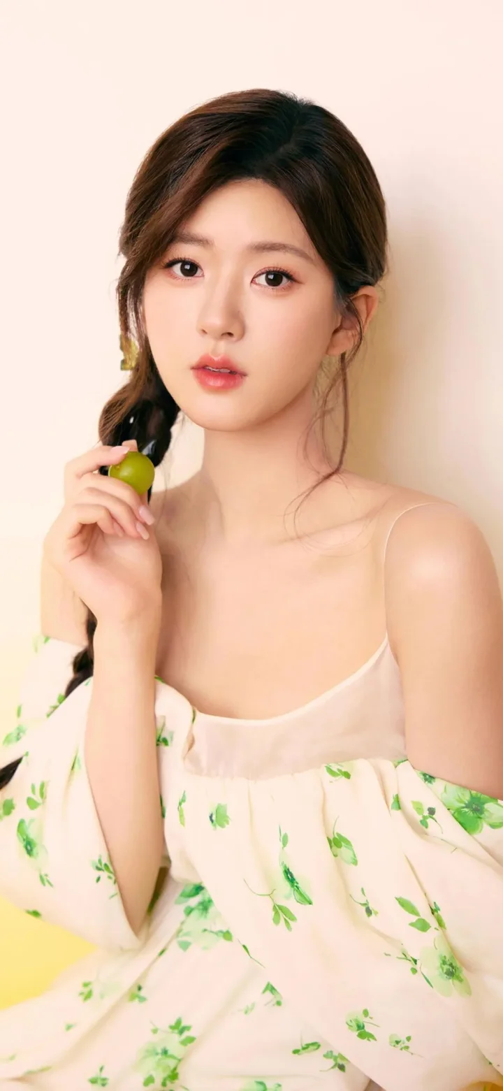 一位成年女性身穿浅色花卉连衣裙，手持一颗绿色水果面对镜头。