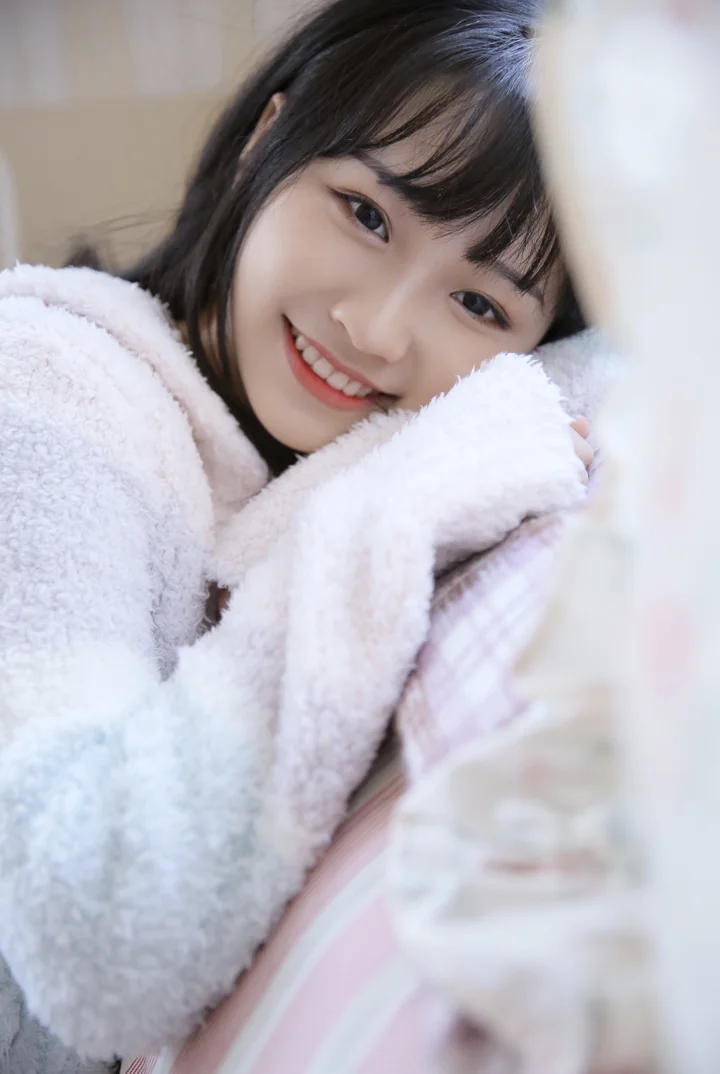 一位短发女子裹着蓬松的浅色毛毯，面带微笑地靠近镜头。