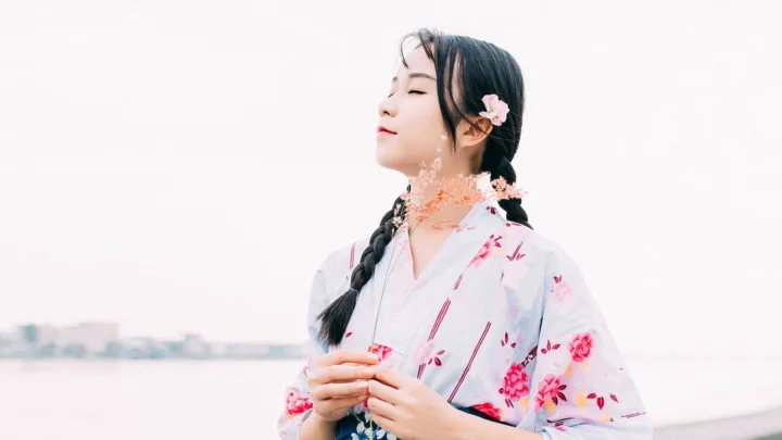 一名闭着眼睛、扎着辫子并佩戴花饰的女子站在水边。