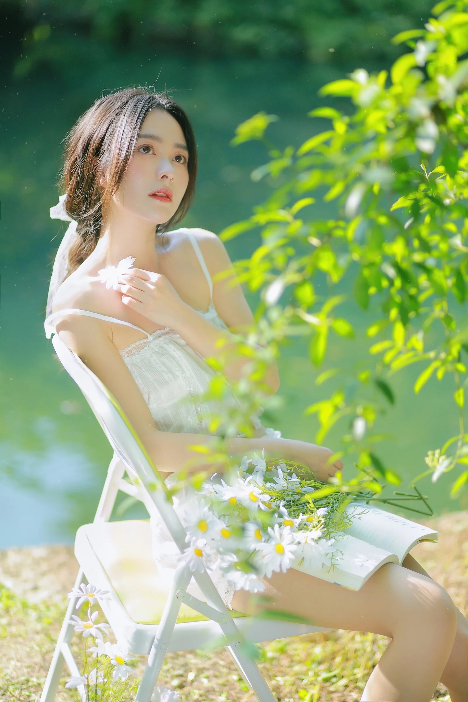 한 여성이 야외 의자에 앉아 흰 꽃을 들고 밝은 초록 잎사귀에 둘러싸여 있다.