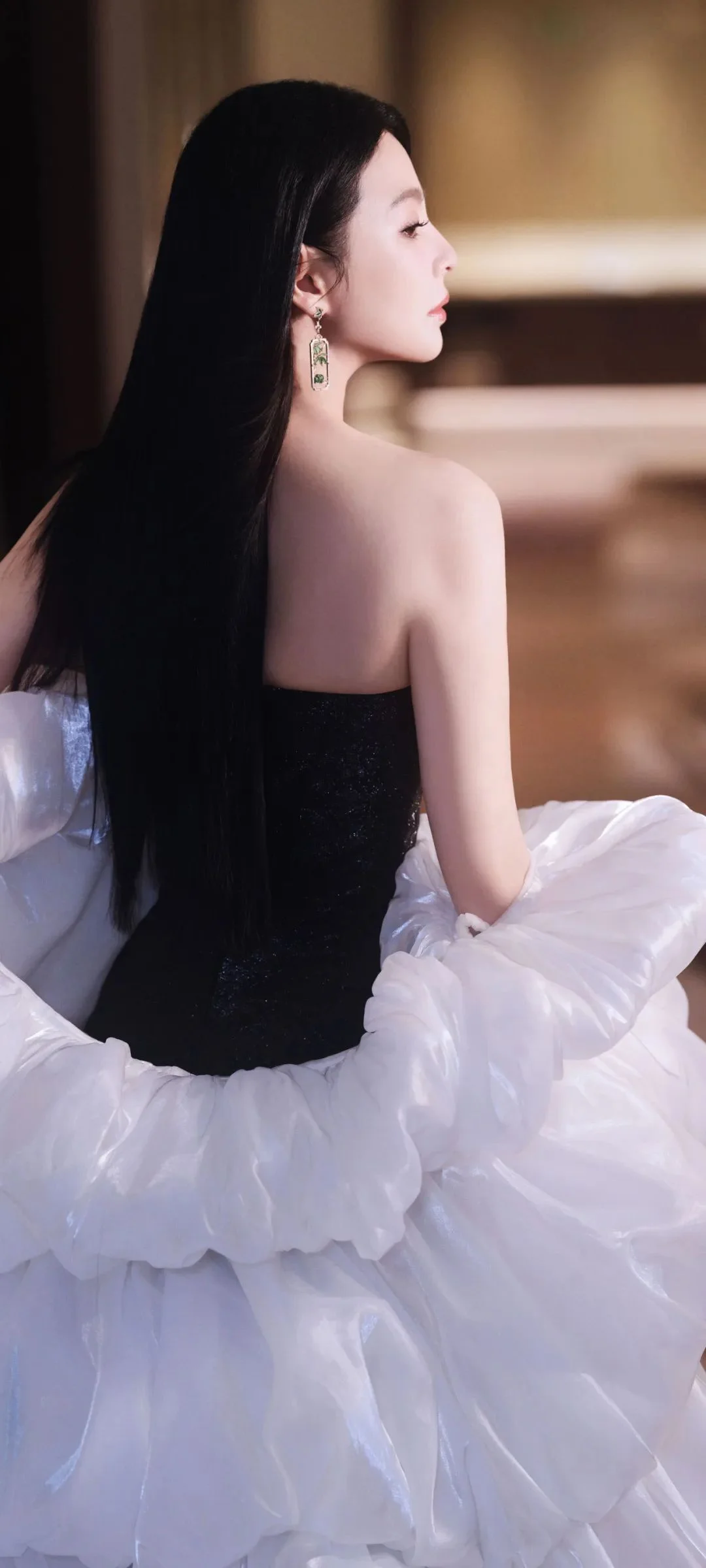 검은색 상의와 풍성한 흰색 치마를 입은 성인 여성이 실내에서 옆모습으로 앉아 있습니다.