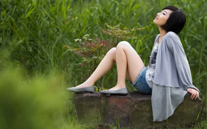 一名女子坐在青草丛中的石台上仰望天空。