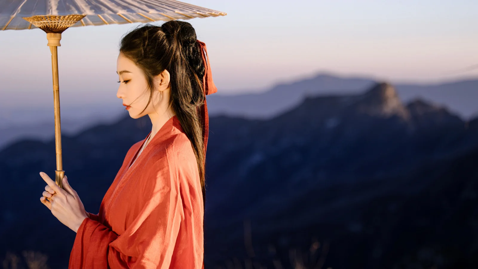 一名身穿传统服饰的女子在山景前撑着伞。