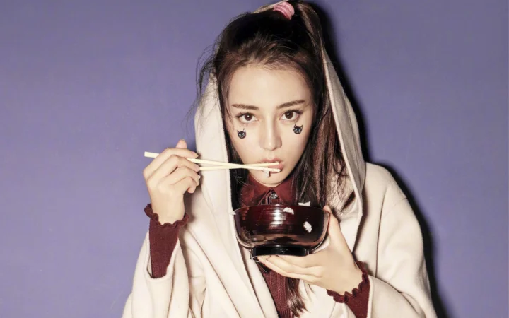 一名长发女子在紫色背景前手持碗和筷子。