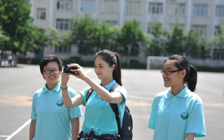 三名身穿浅蓝色上衣的女性站在户外，其中一人手持相机拍摄。
